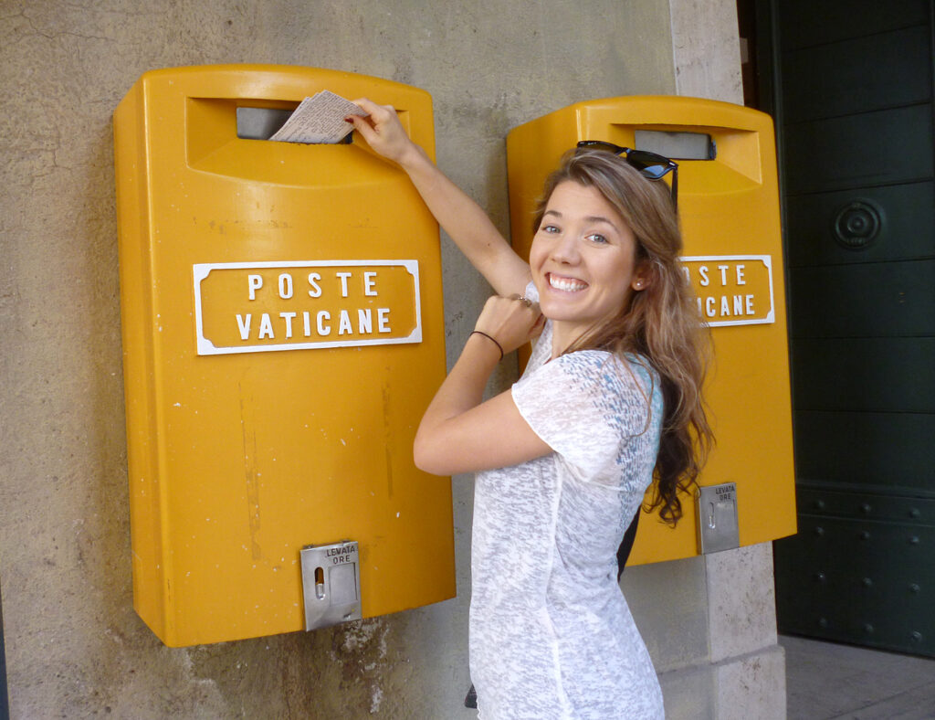 Nessie Early dropping mail into a yellow mail drop box.