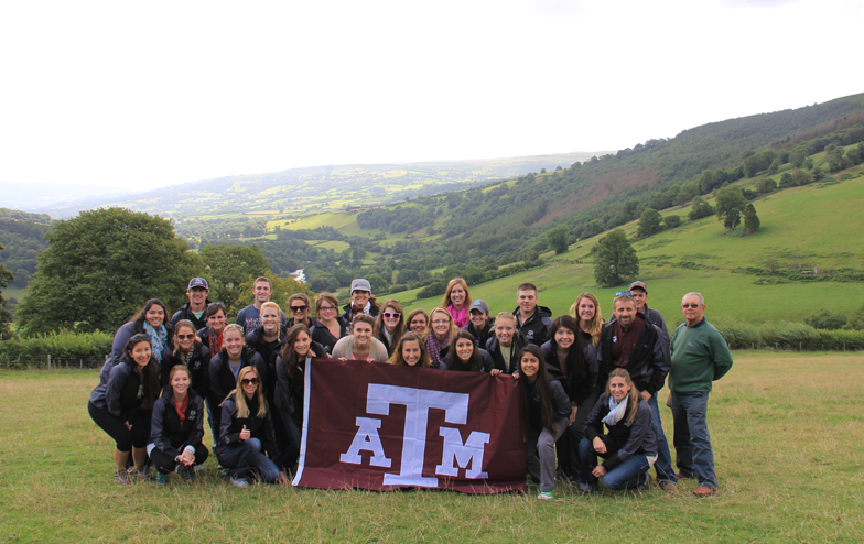 A group of students in a meadow with the Aggie Flag