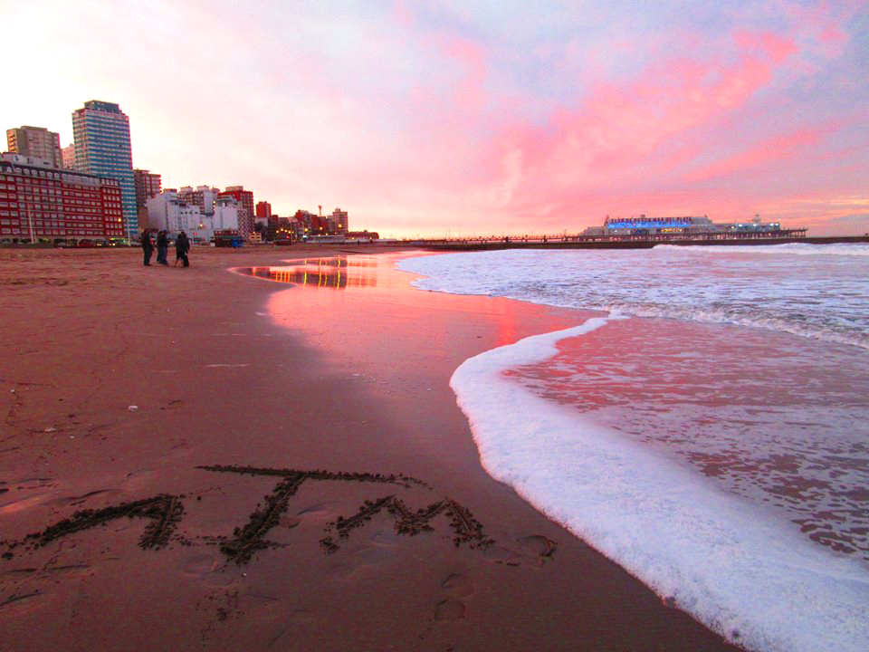 A beach scene with the Texas A&M "ATM" logo written in sand.