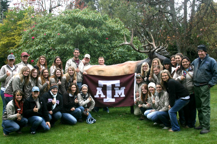 Group of students with the A&M flag in front of an elk statue.