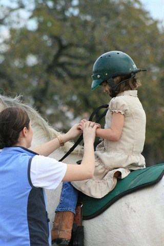 A child getting assistance from an adult on how to ride a horse.