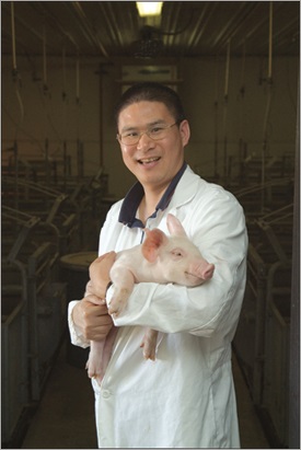 Dr. Guoyao Wu in a lab coat holding a pig.