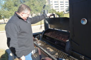 Dr. Davey Griffin checking meat in a barbecue pit.