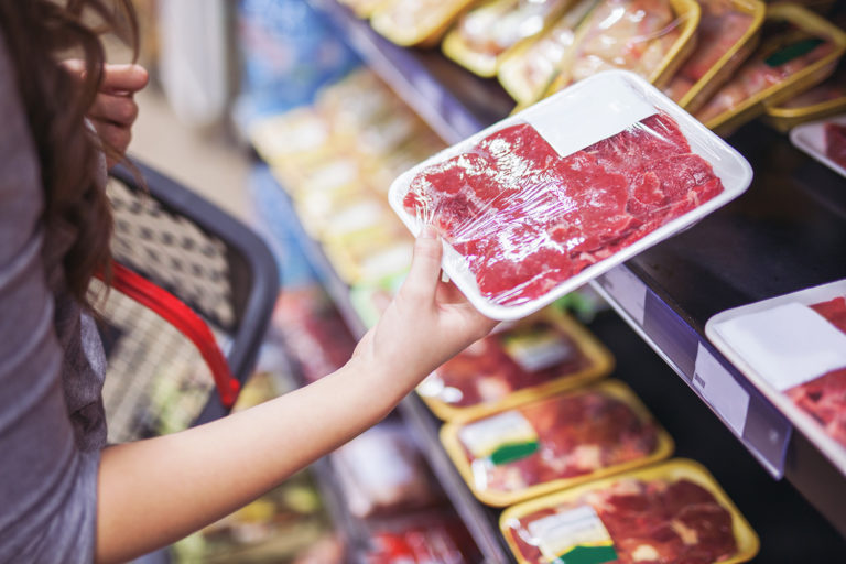A woman picks up meat from a grocery store meat counter. She is looking at the quality of the meat.