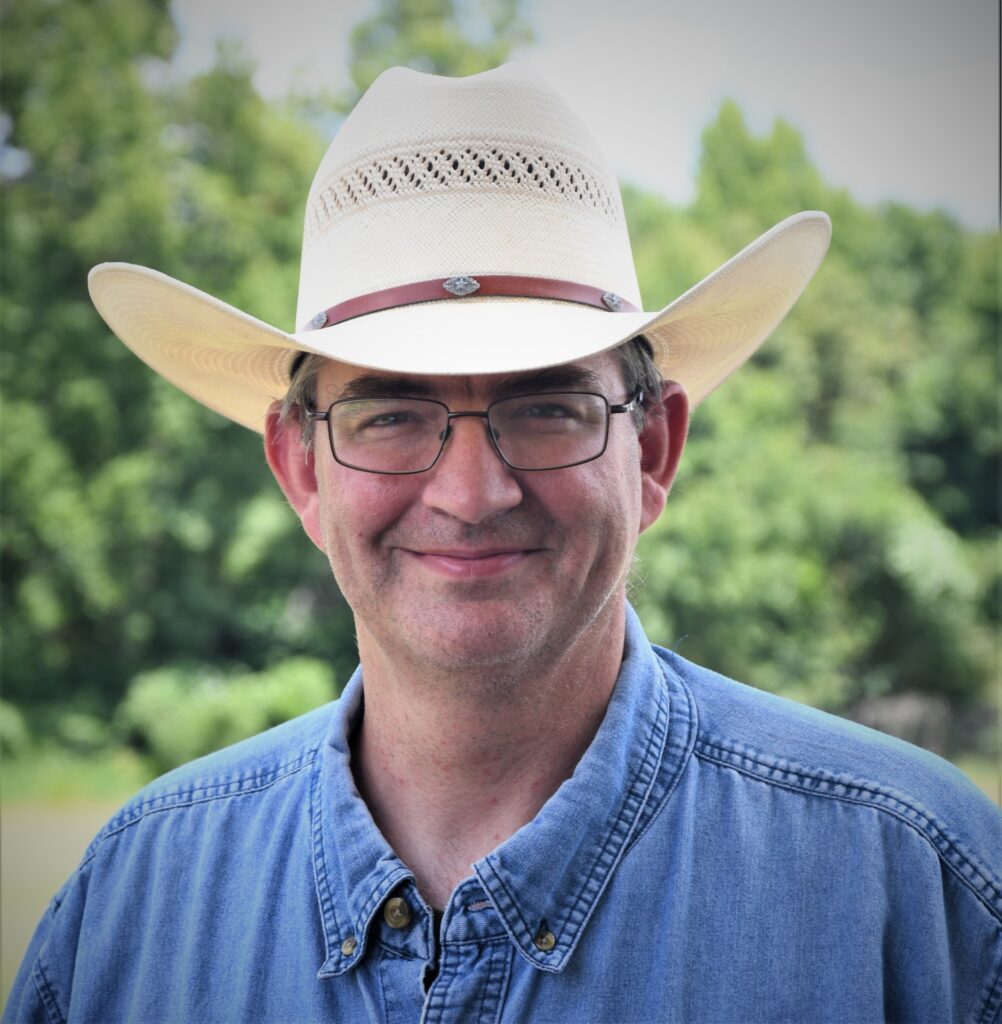 Man smiling in a cowboy hat involved in cattle research.