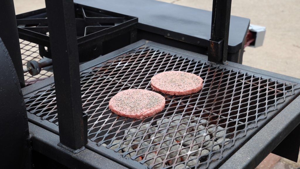 Raw ground beef patties on a grill being cooked.