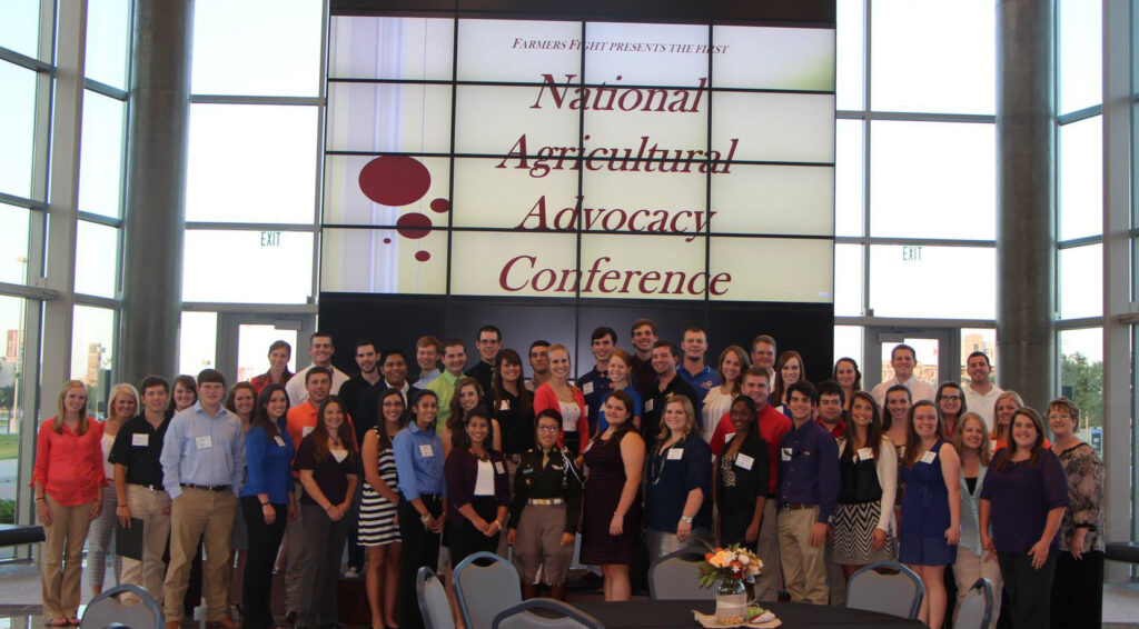 A group standing in front of the video screen with the words "National Agricultural Advocacy Conference" inside the Shirley and Joe Swinbank '74 AgriLife Center