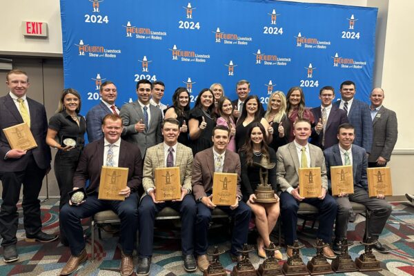 Students sit and stand in front of backdrop holding plaques and banners at a judging competition.