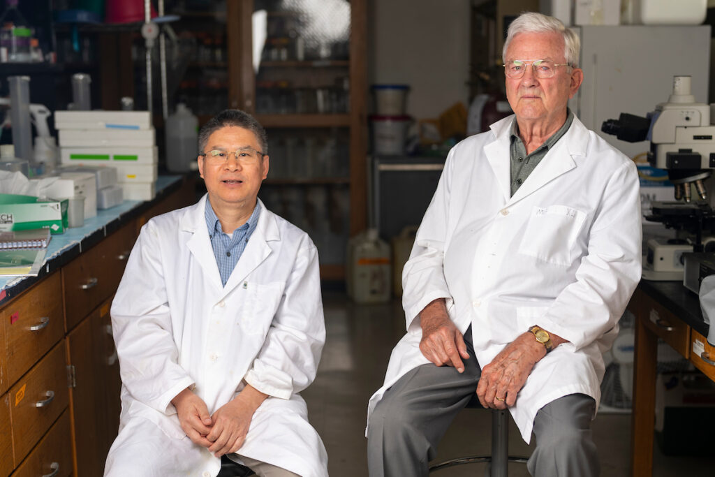 Two animal science researchers, Guoyao Wu and Fuller Bazer, sit in a lab setting with their white coats on.