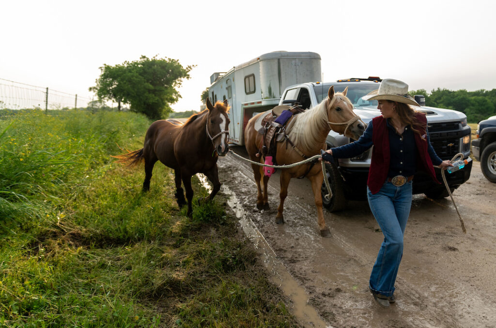 A woman leading two horses along a dirt road