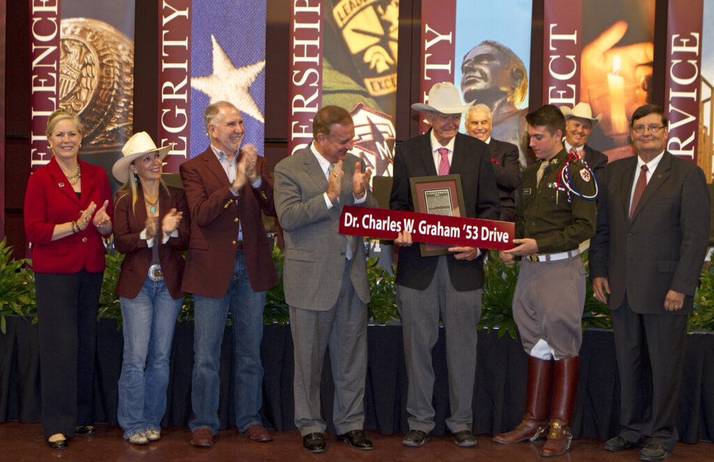 The road leading up to the Equine Complex has been named after Dr. Charles “Doc” Graham ’53. Congratulating Graham (holding sign), from left, are Dr. Eleanor Green, the Carl B. King dean of the College of Veterinary Medicine and Biomedical Sciences; Marti Young and her husband, Texas A&M president Dr. Michael Young; Dr. John Sharp, chancellor of the Texas A&M University System; student regent Alvaro “Gabe” Pereira; and Dr. Mark Hussey, dean and vice chancellor of the College of Agriculture and Life Sciences. (Photo by Kate Bradley.)