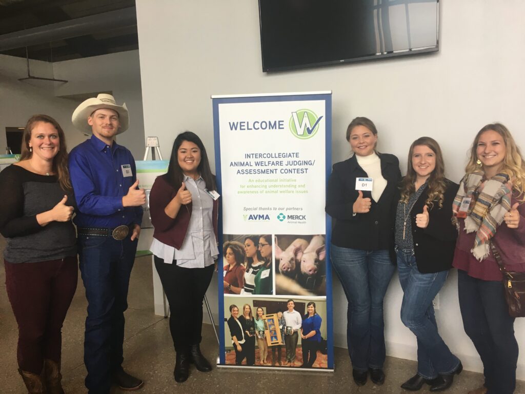 Students posing for the camera with a welcome sign between the middle two students.