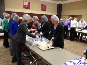 Members of the Saddle and Sirloin Club packing food packages with a group of other people.