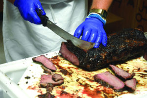 A person cuts a brisket into slices.
