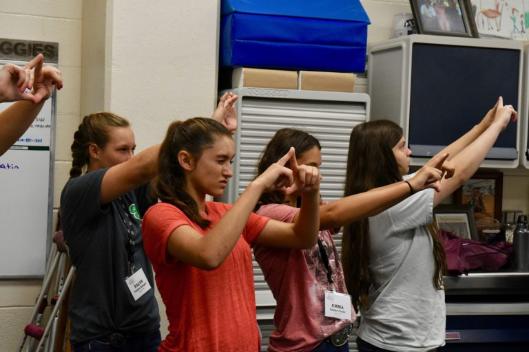 Four students looking forming triangle with one hand and looking through it as part of test to see which eye is dominate.