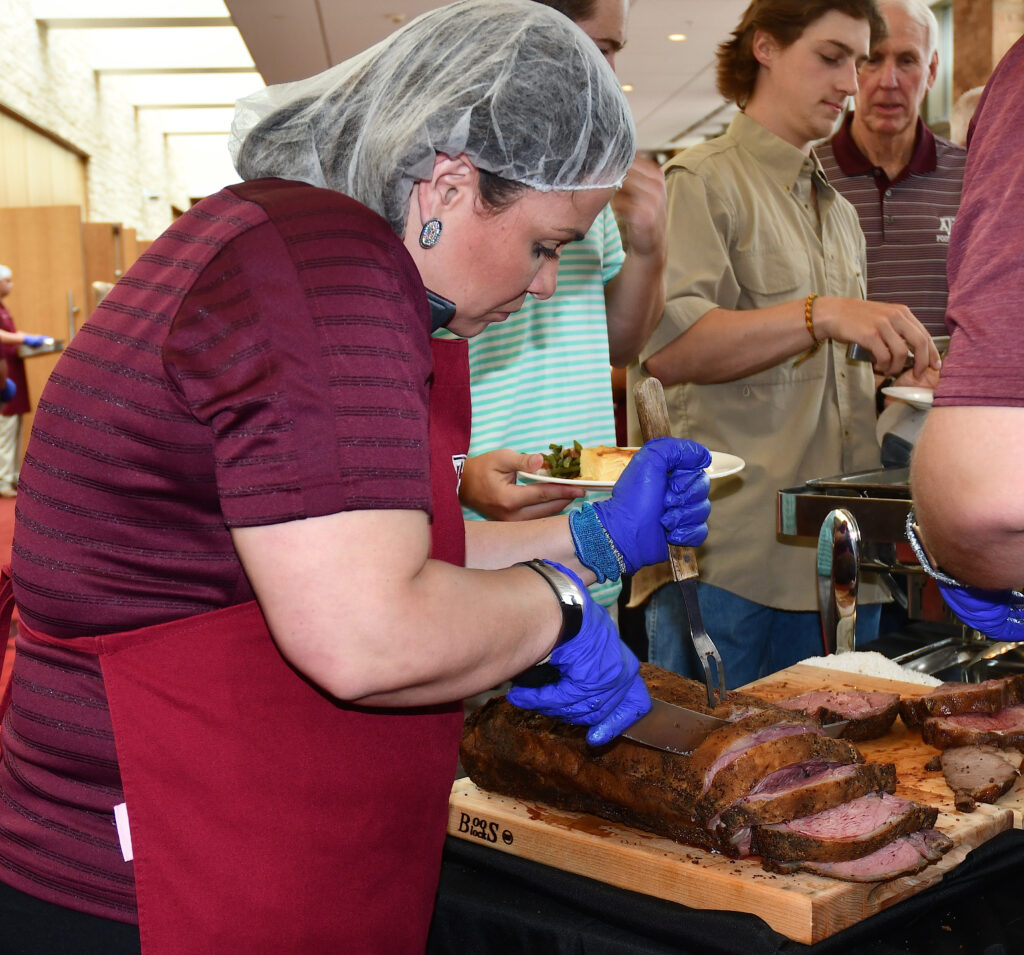 A woman is cutting prime rib for participants.