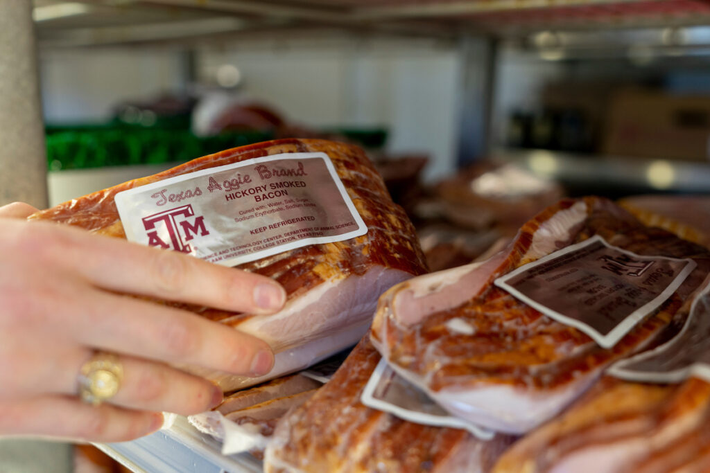 Close-up image of a hand removing a package of bacon from a shelf