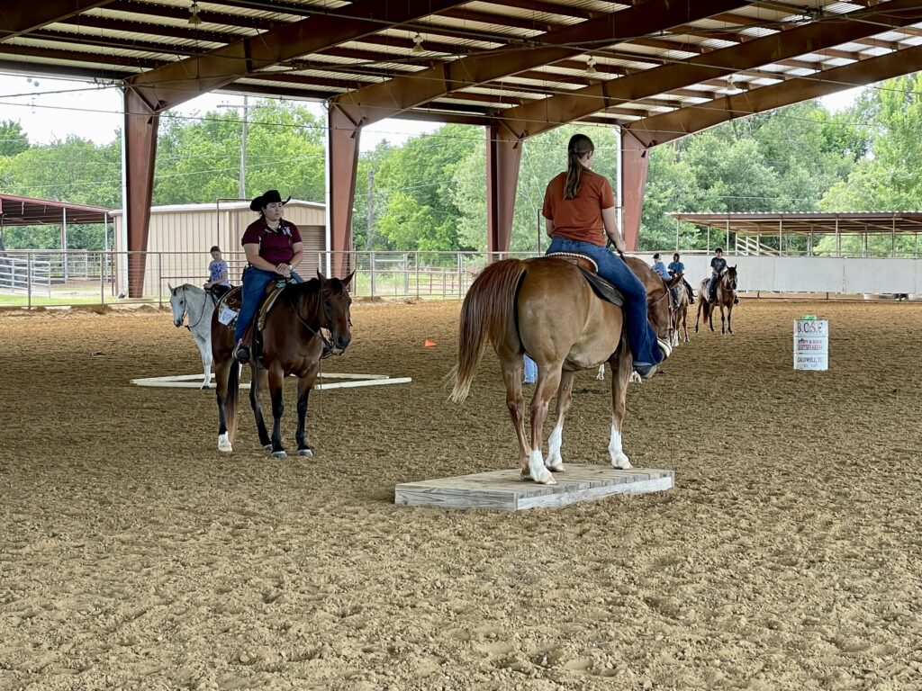 People on horses in an open air arena.