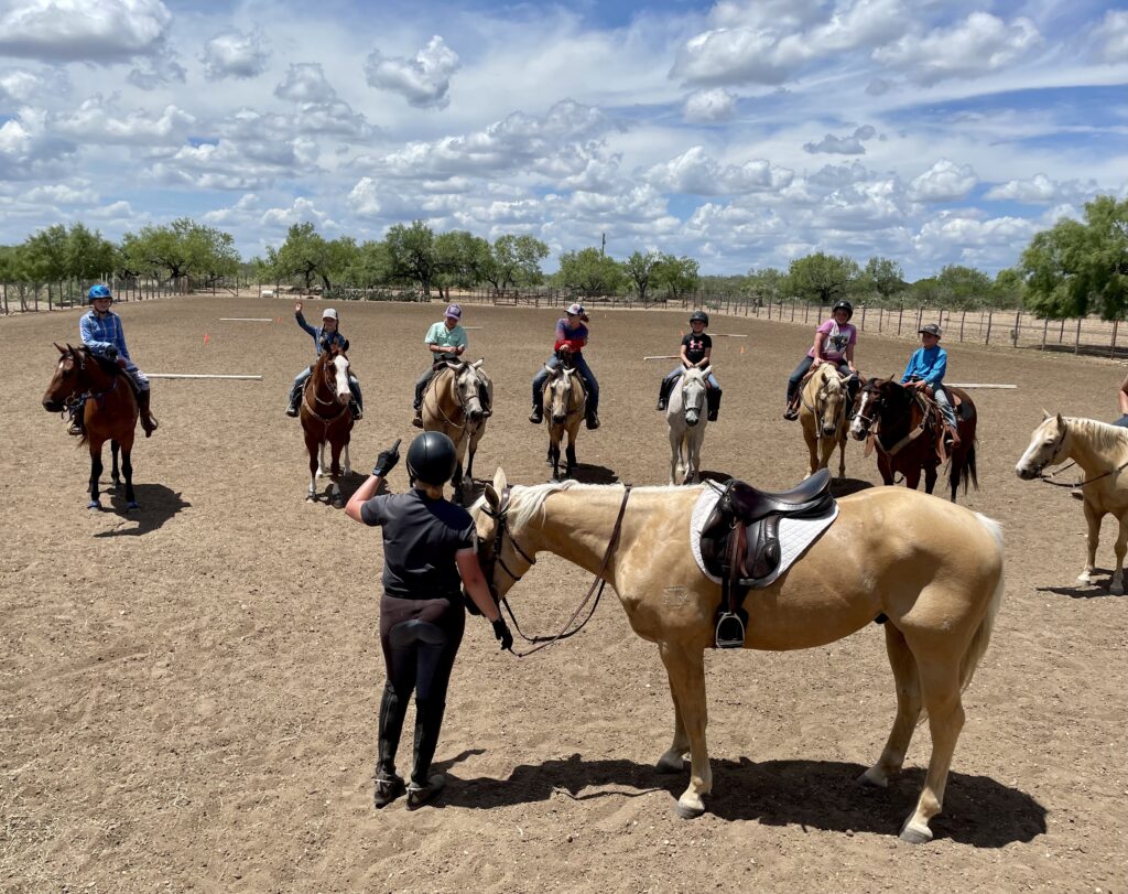 An instructor talking to kids on horses.