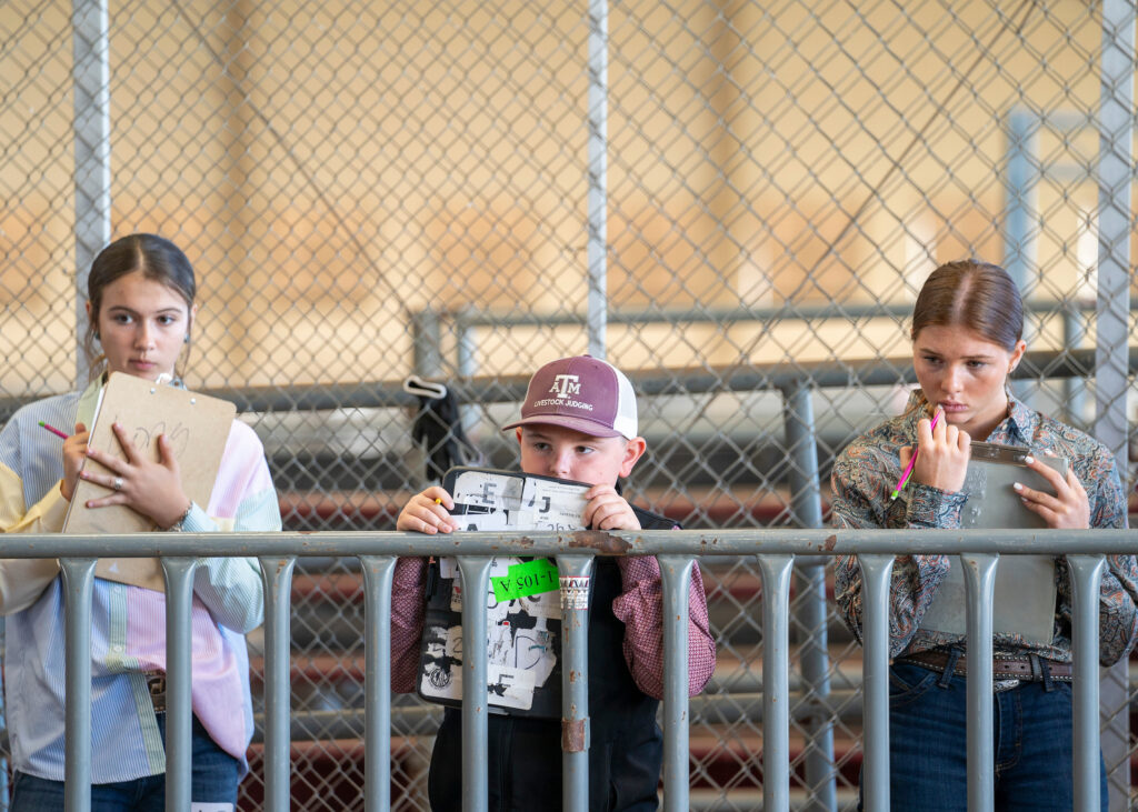 Three young students in a livestock judging contest, thinking deeply and taking notes on clipboards.