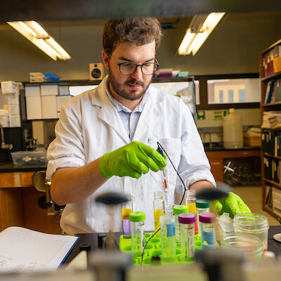 Man using blue gloves and white lab coat while doing some testing on different science equipment. 